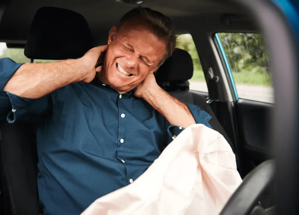 A driver holding their neck in pain beside a lightly damaged car.