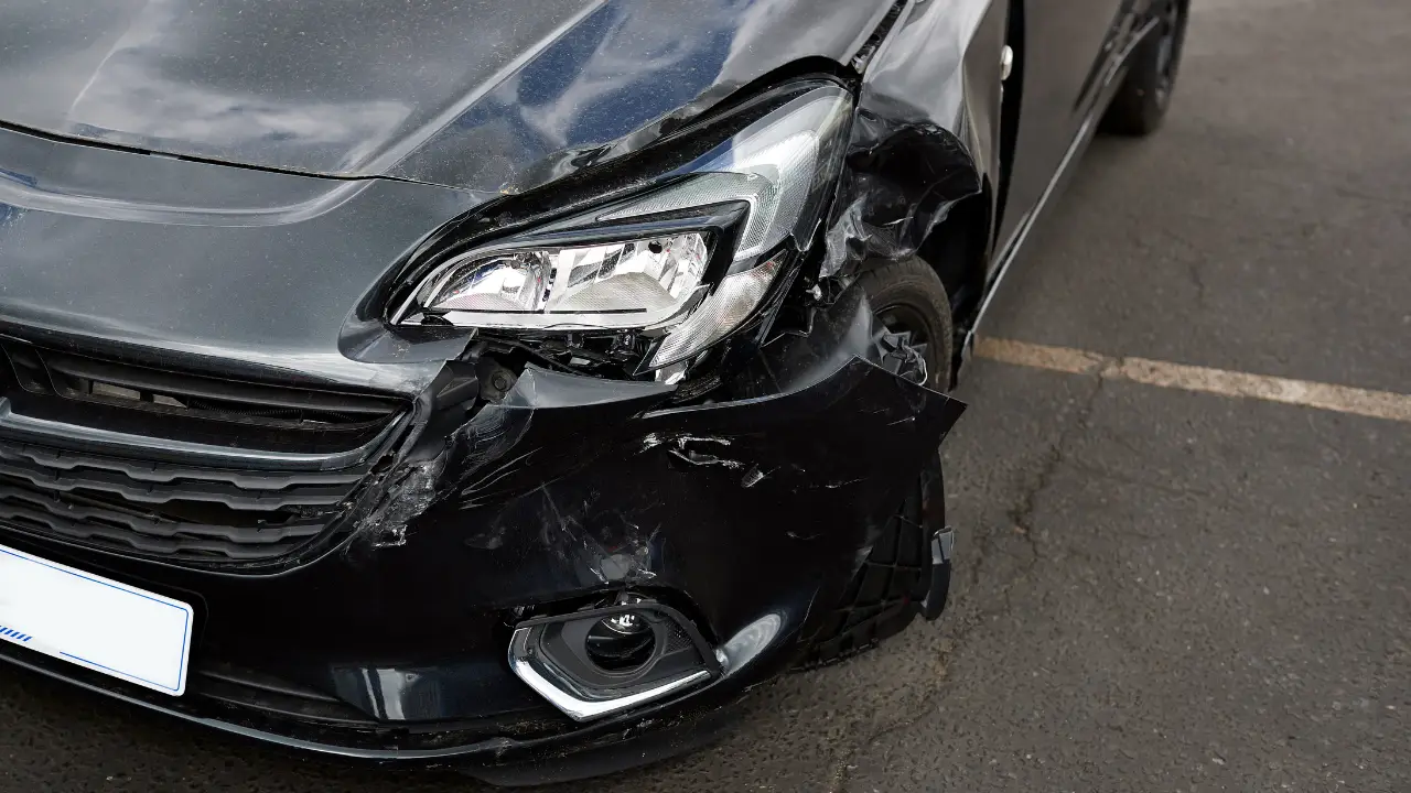 Close-up of a damaged car headlight in a parking lot showing cracks and scratches.