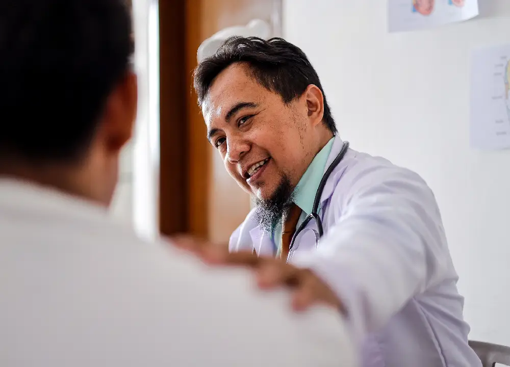 A doctor gently touches a patient’s shoulder, expressing empathy and support during a medical appointment.