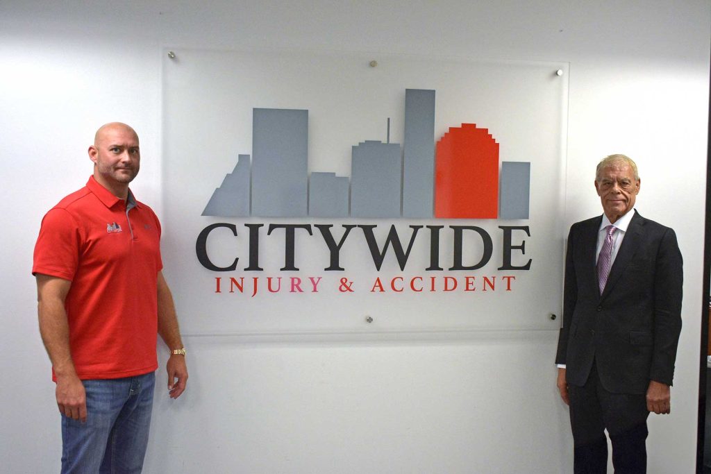 Two men standing in front of the CityWide Injury & Accident logo on a wall