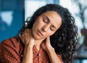 A woman sits in a doctor’s office holding her neck in pain from a whiplash injury.